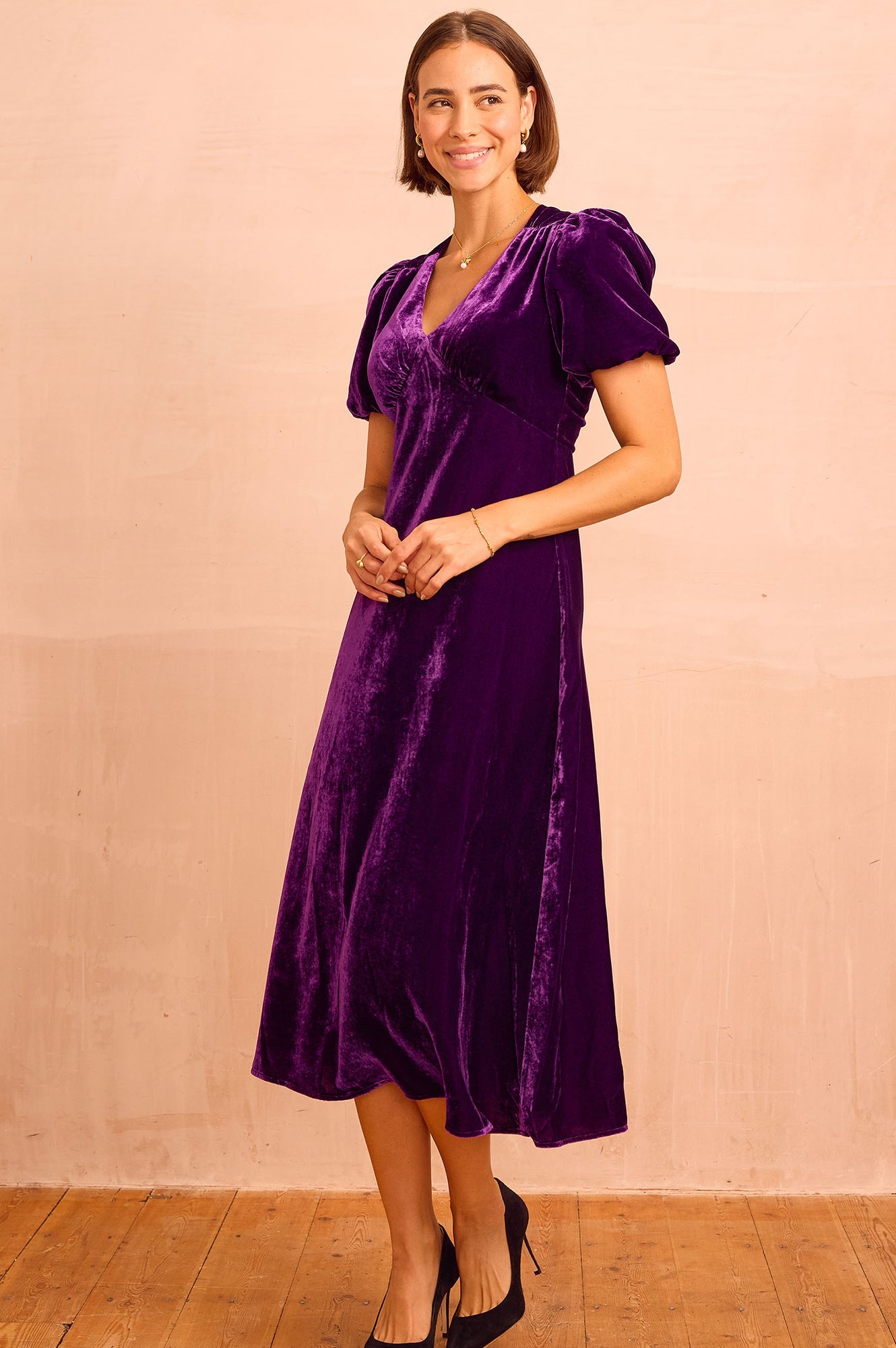 Purple velvet midi dress with V-neckline, short puff sleeves, fitted bodice, and flowing skirt.