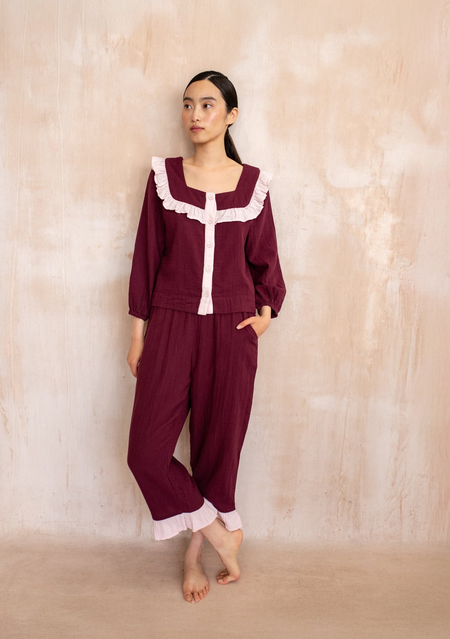 Burgundy pyjama set with soft pink trim, featuring a button-up top with ruffled neckline and matching trousers with ruffle hem.