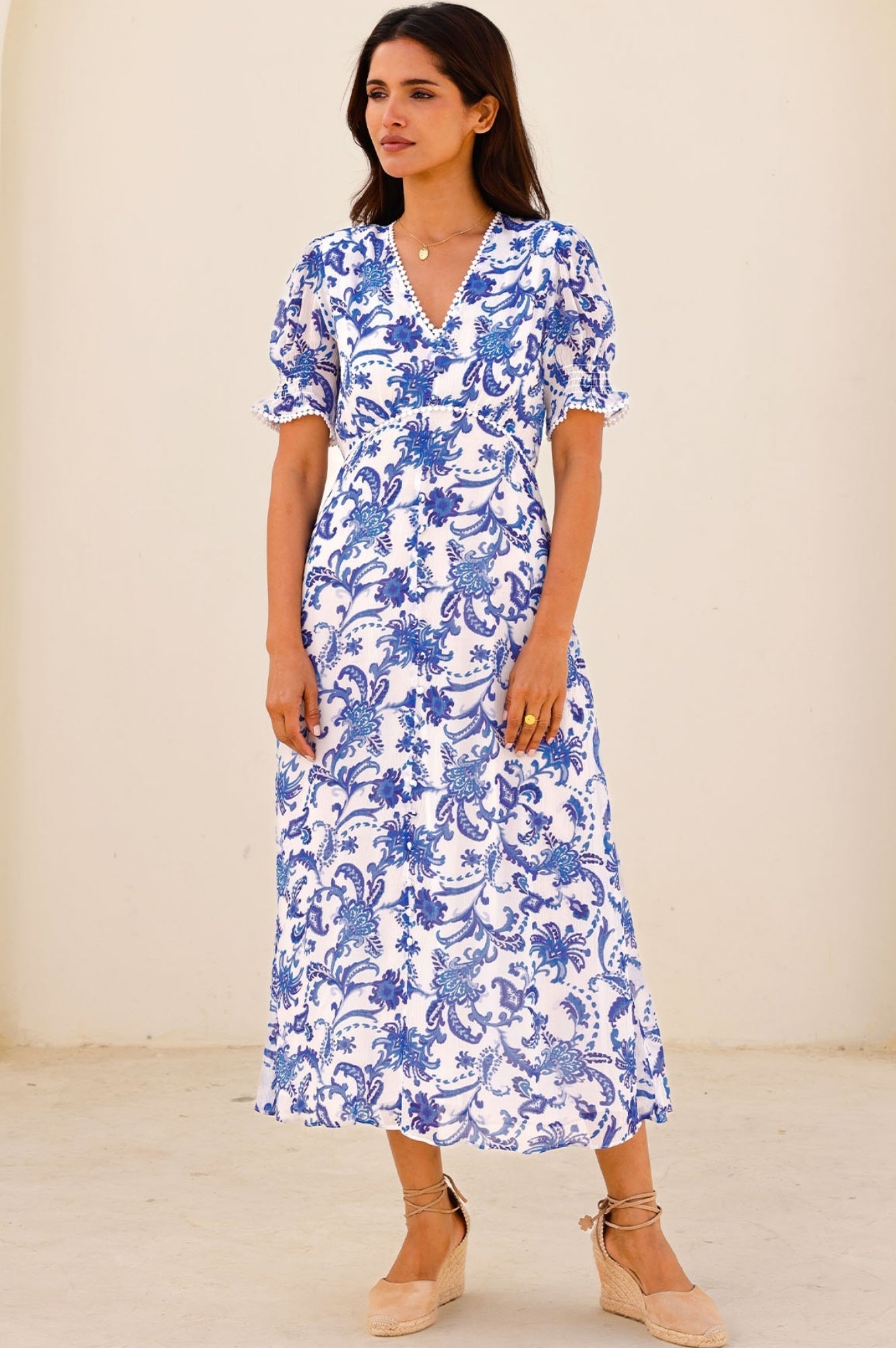 White midi dress with blue floral print, V-neckline, short puff sleeves, and fitted waist.