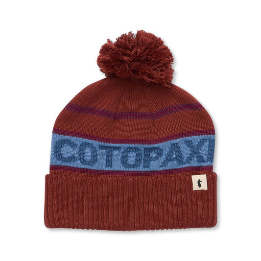 Browny red pom pom beanie with Cotopaxi logo knitted in blue.