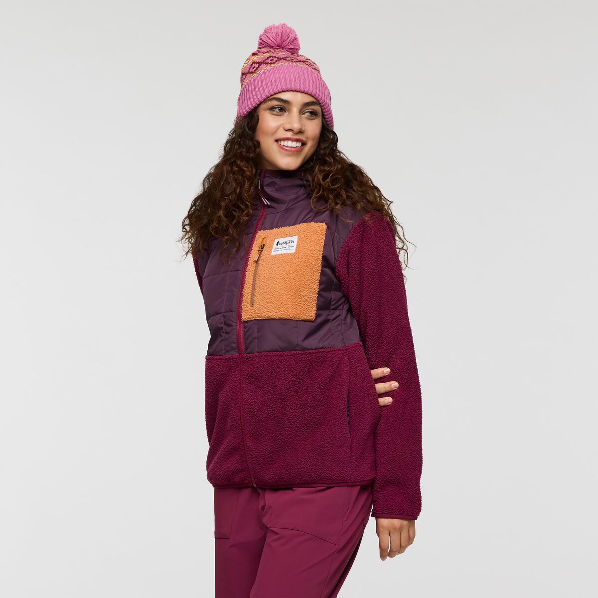 Rich burgundy and deep purple two-tone puffer jacket with fleece sleeves and orange feature pocket on chest, by Cotopaxi.