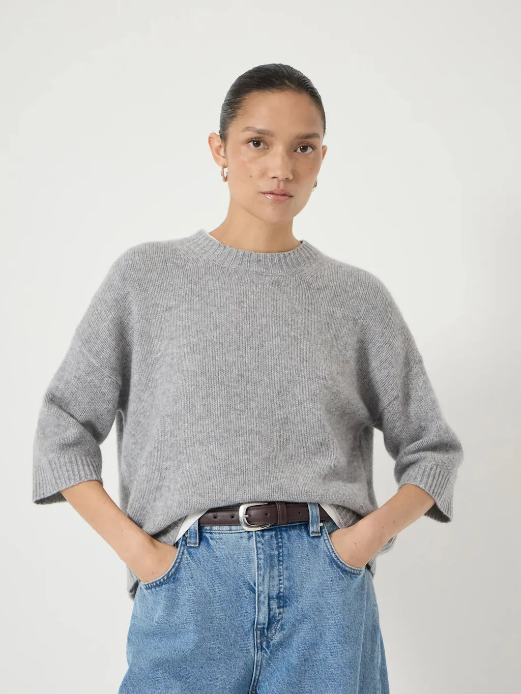 Soft mid-grey relaxed knit sweater with a round neckline and elbow-length sleeves, styled with light blue jeans.