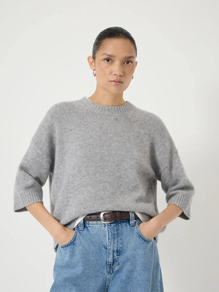 Soft mid-grey relaxed knit sweater with a round neckline and elbow-length sleeves, styled with light blue jeans.