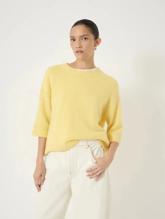 Soft buttery yellow knit sweater with a round neckline and elbow-length sleeves, styled with off-white trousers.
