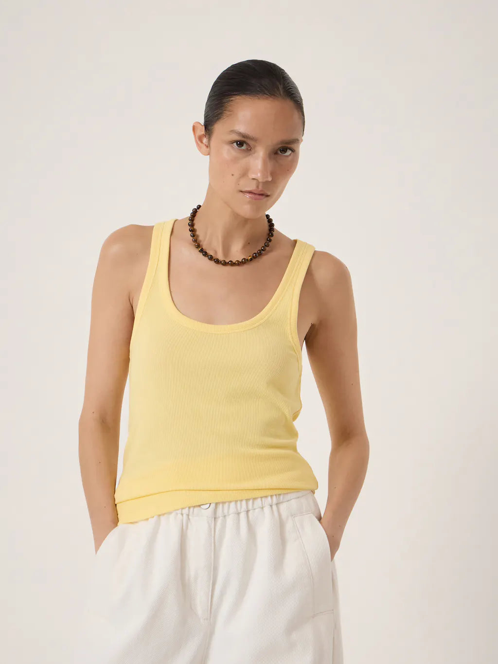 Pale buttery yellow ribbed tank top with a scoop neckline and slim fit.