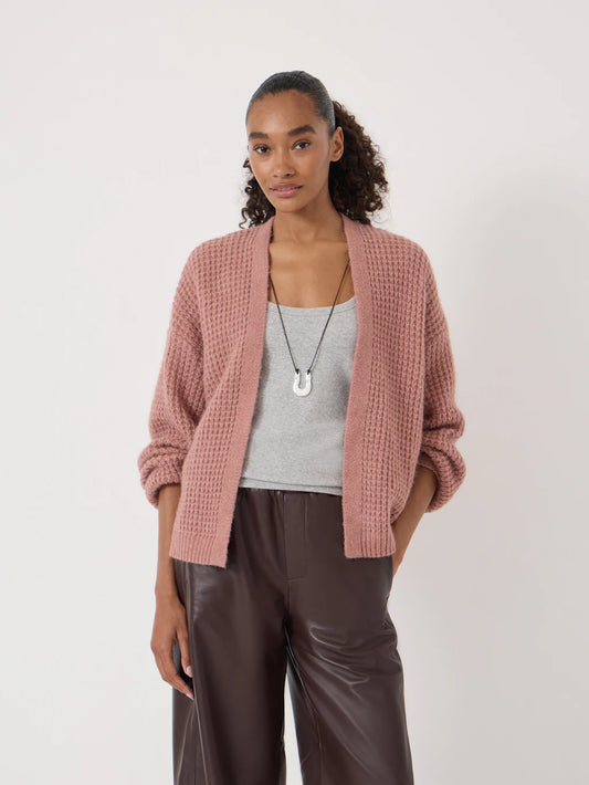 A woman modeling a dusty rose waffle-knit cardigan over a light gray tank top and dark brown wide-leg trousers, standing against a plain off-white studio background.