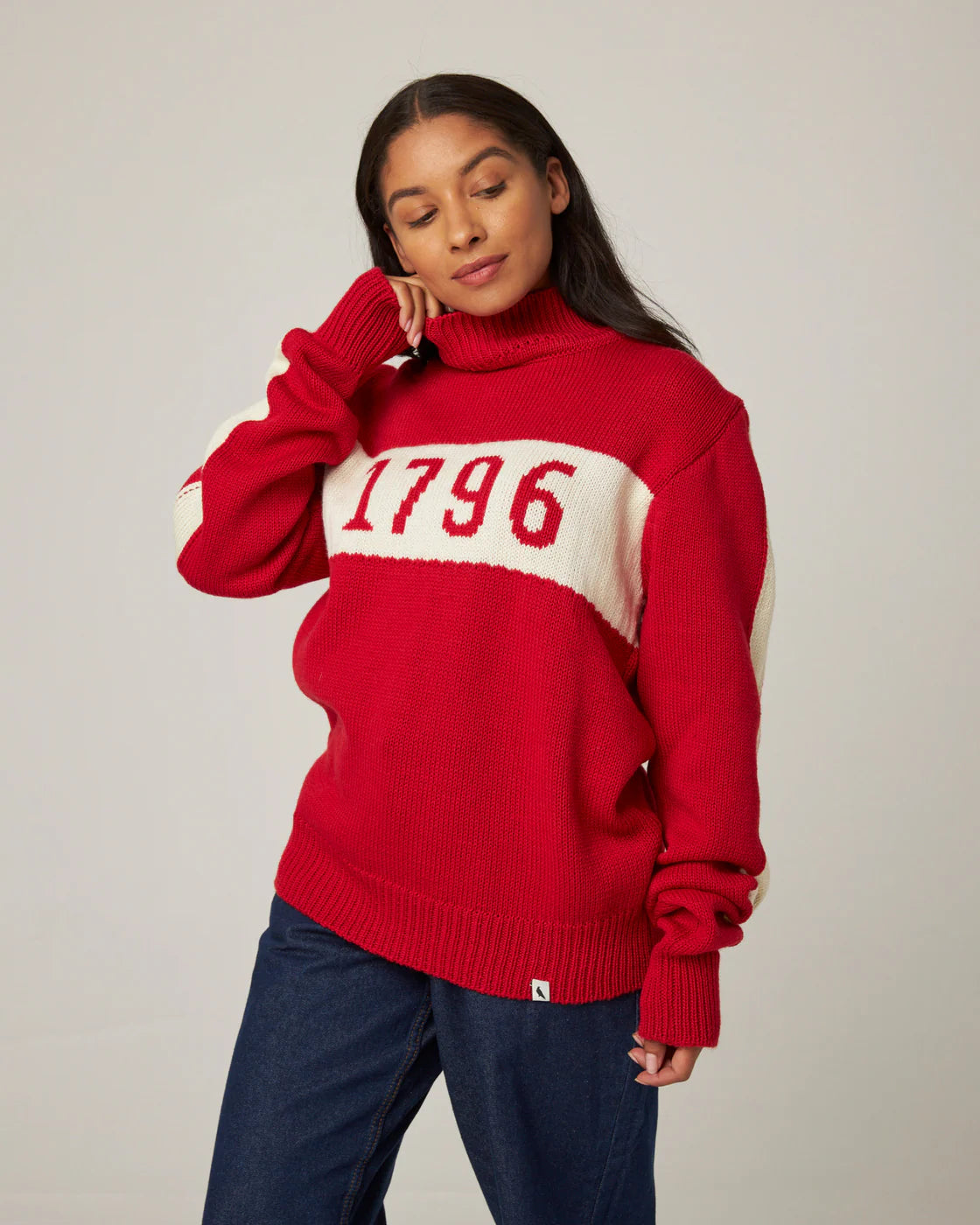 Model wearing a bright red merino wool knitted polo neck sweater with cream stripe and '1796' knitted logo. Made by Peregrine Clothing and filtered for the Clear Spring, Warm Spring, and Clear Winter colour seasons.