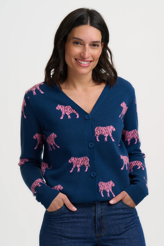 A woman wearing a navy blue cardigan with pink tiger-patterned motifs, paired with dark blue jeans, against a plain white studio background.