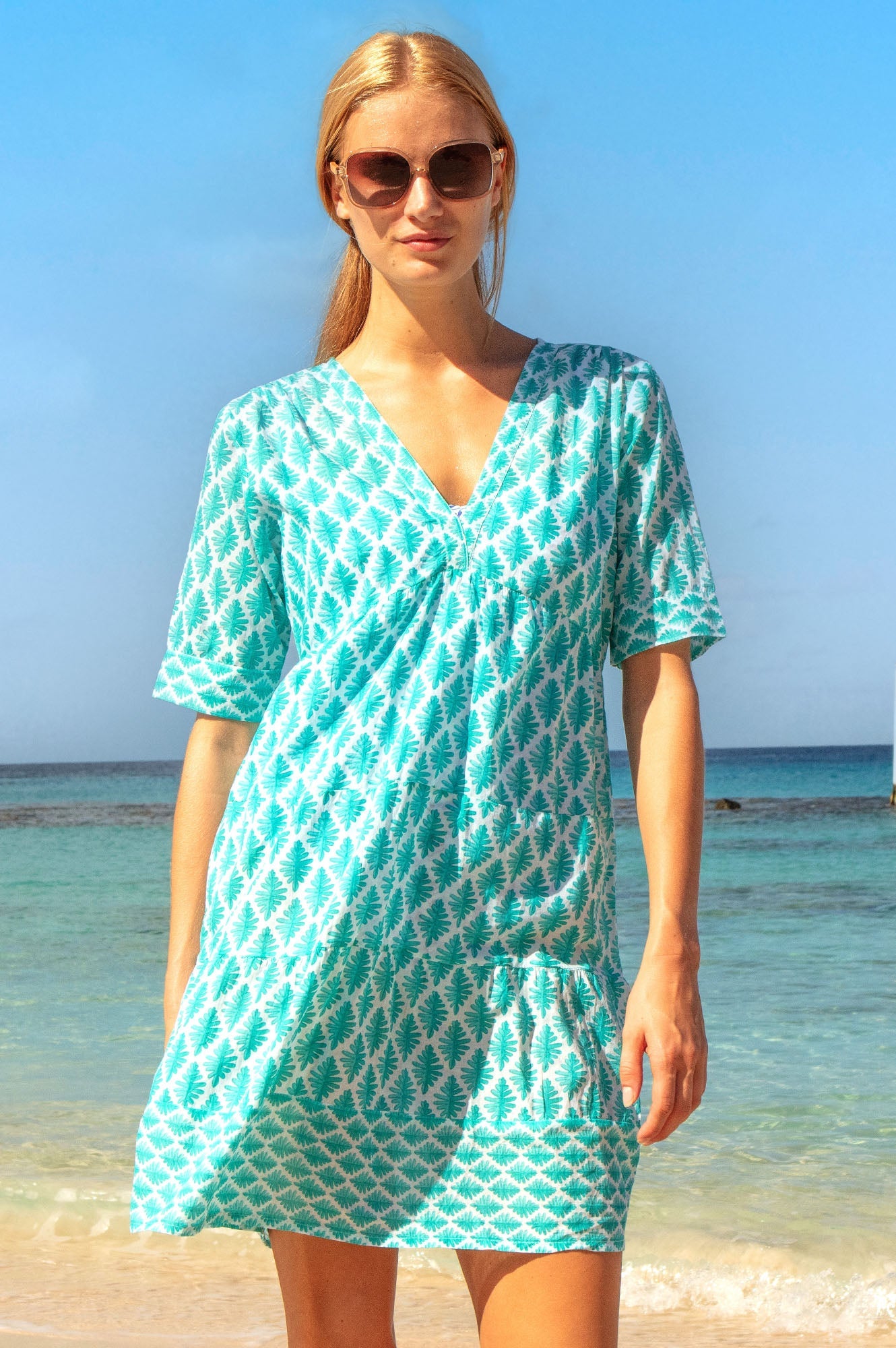 Turquoise patterned mini dress with V-neckline, short sleeves, and white geometric print.