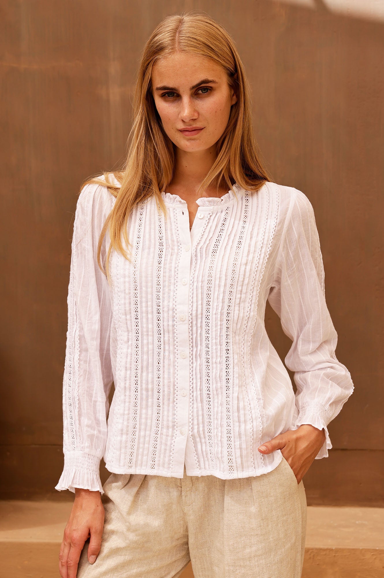 White lace blouse with pintuck detailing, ruffle neckline, button front, and long sleeves.