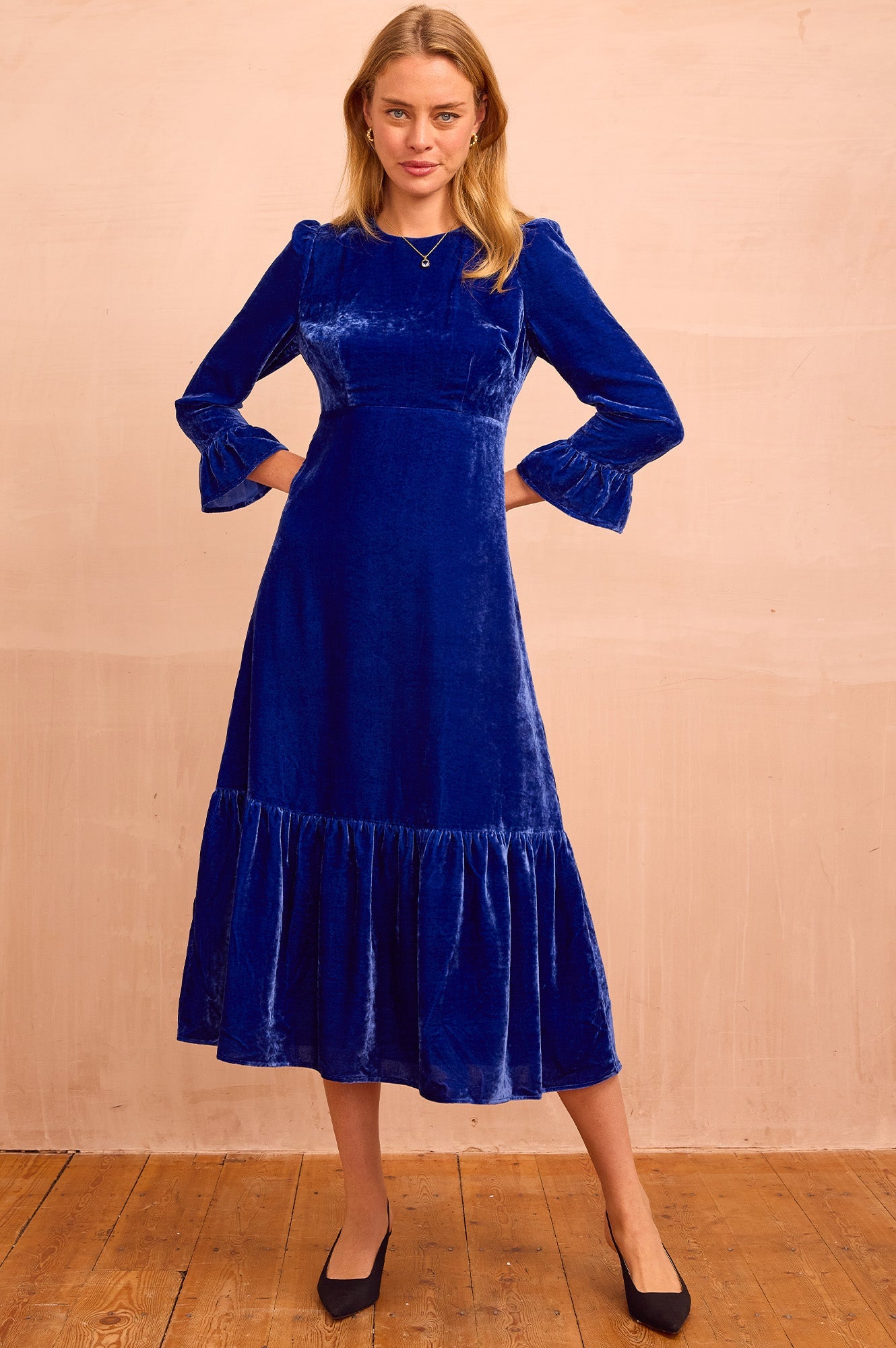 Royal blue velvet midi dress with round neckline, long sleeves with fluted cuffs, fitted waist seam, and gathered hem.
