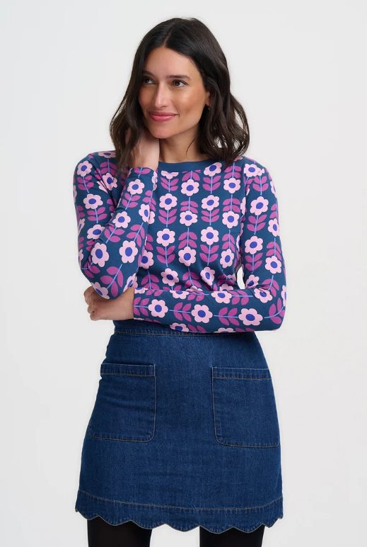 A woman modeling a navy blue long-sleeve top with a pink and white floral pattern, paired with a dark blue denim mini skirt, against a plain white studio background.