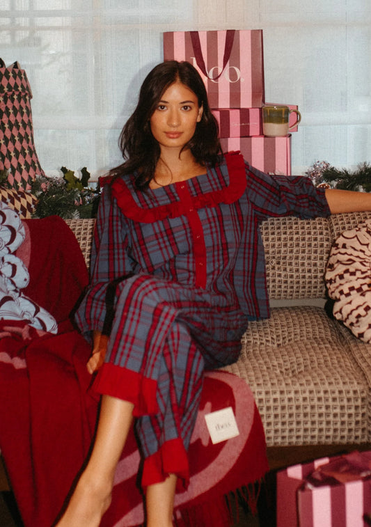 Woman in red and navy blue plaid pyjamas sitting on a couch with decorative items around. Pyjamas are by TBCo and filtered for the Cool Winter, Clear Winter, and Deep Winter colour seasons by Shop My Palette.