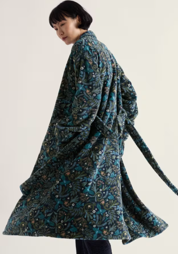 A model wearing a long-sleeved, belted robe with a dark teal and black botanical pattern, photographed against a solid off-white background.