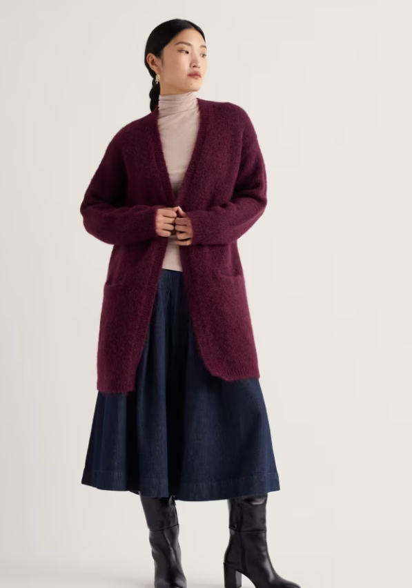 Model wears deep burgundy cardigan over a turtleneck top and denim skirt.