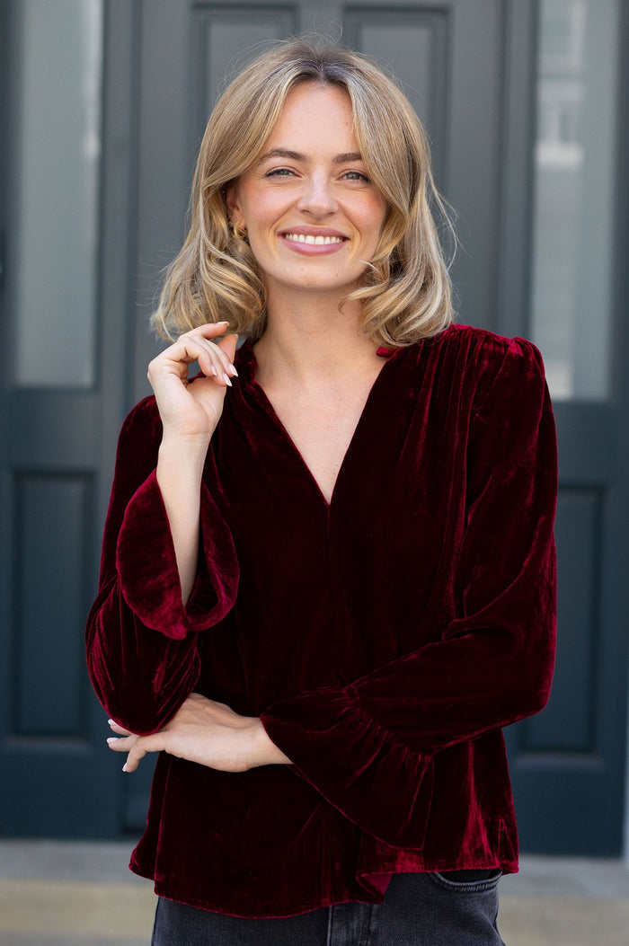 Burgundy velvet blouse with v-neck and flowing sleeves.