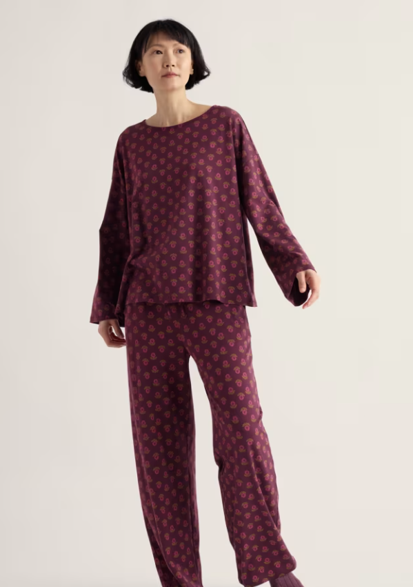A woman modeling a two-piece pajama set consisting of a long-sleeve top and matching pants, both in a deep burgundy color with a small pink floral pattern, against a plain off-white background.