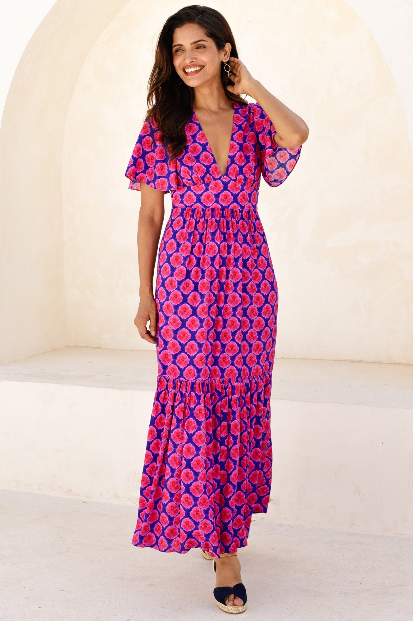 Purple and pink floral maxi dress with deep V-neckline, short flutter sleeves, fitted waist, and tiered skirt.