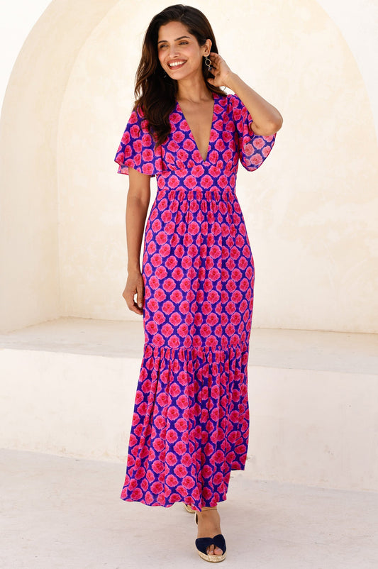 Purple and pink floral maxi dress with deep V-neckline, short flutter sleeves, fitted waist, and tiered skirt.