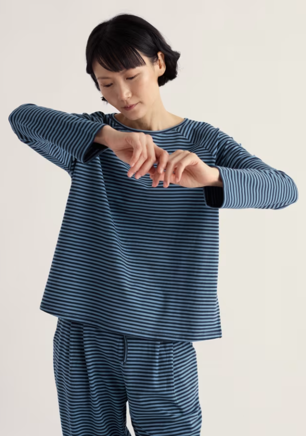 Woman wearing blue striped cotton pyjamas against a beige background.