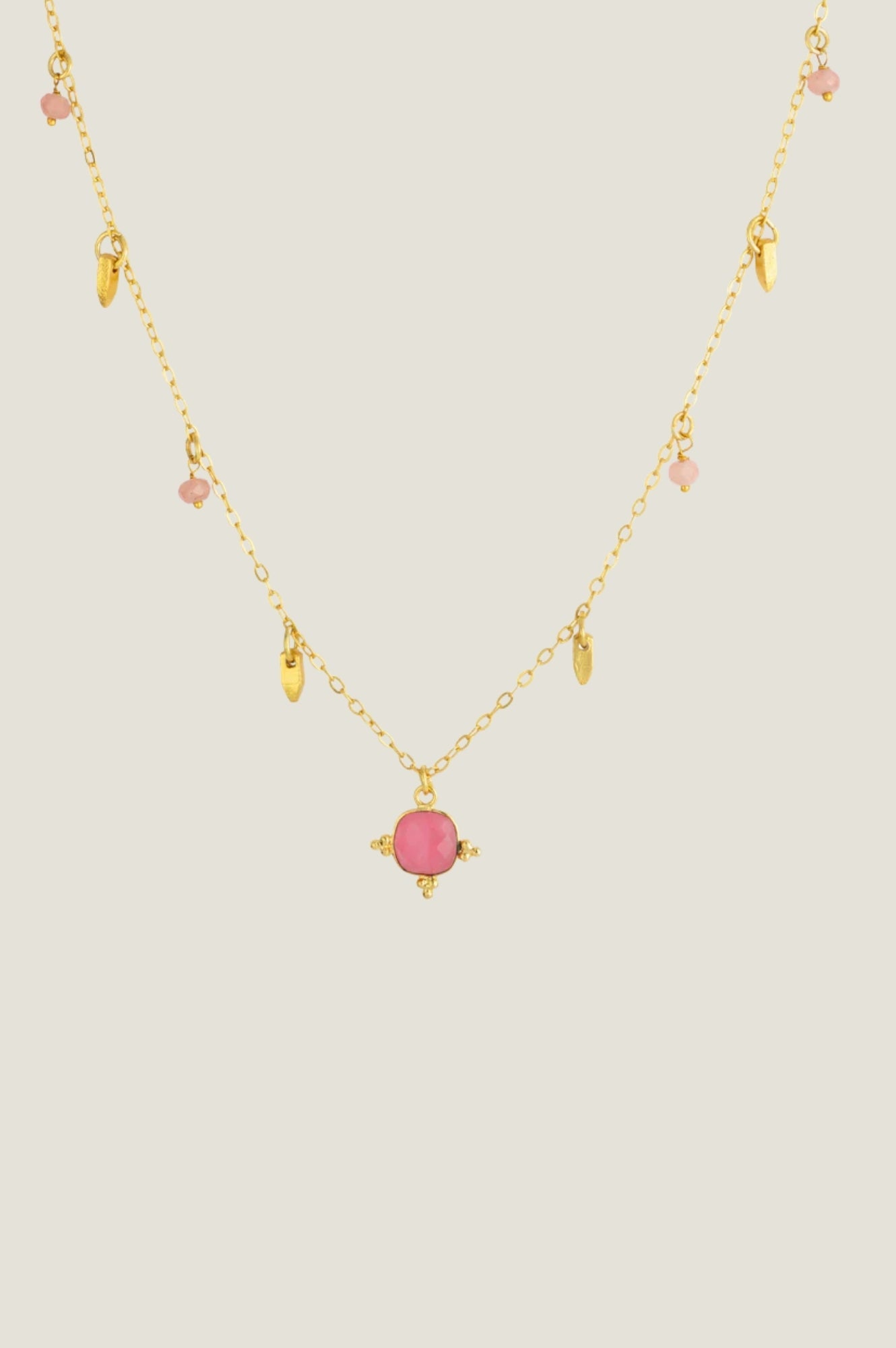 Gold charm necklace with pink gemstone pendant and small gold and pink bead details.