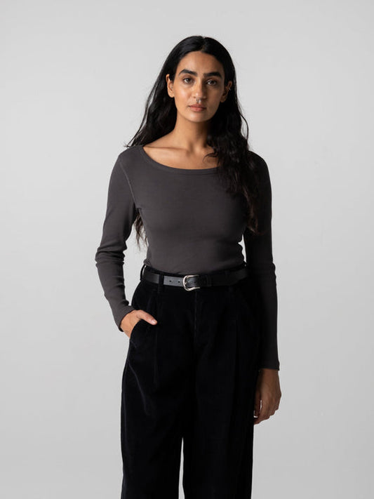 A woman modeling a dark gray long-sleeve top and black wide-leg trousers with a black belt, standing against a light gray studio background.