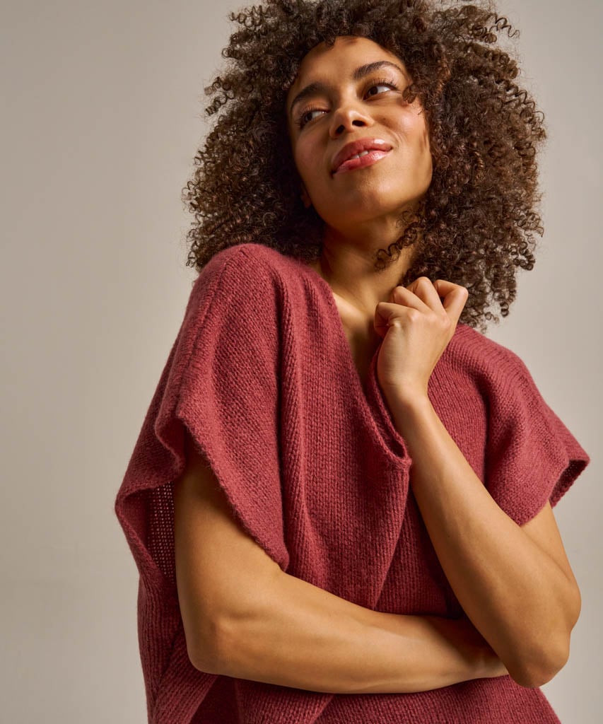 A woman wearing a textured, short-sleeved burgundy knit top, posing against a neutral light grey background.