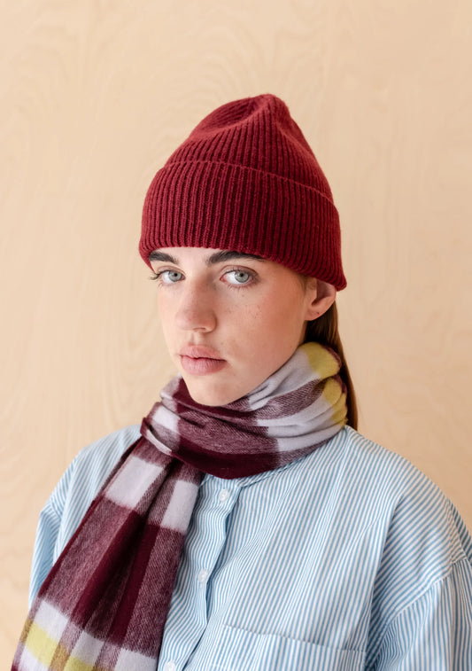 Person wearing a burgundy beanie and plaid scarf against a beige background. Knitwear is by TBCo and filtered for the Deep Autumn colour season by Shop My Palette.