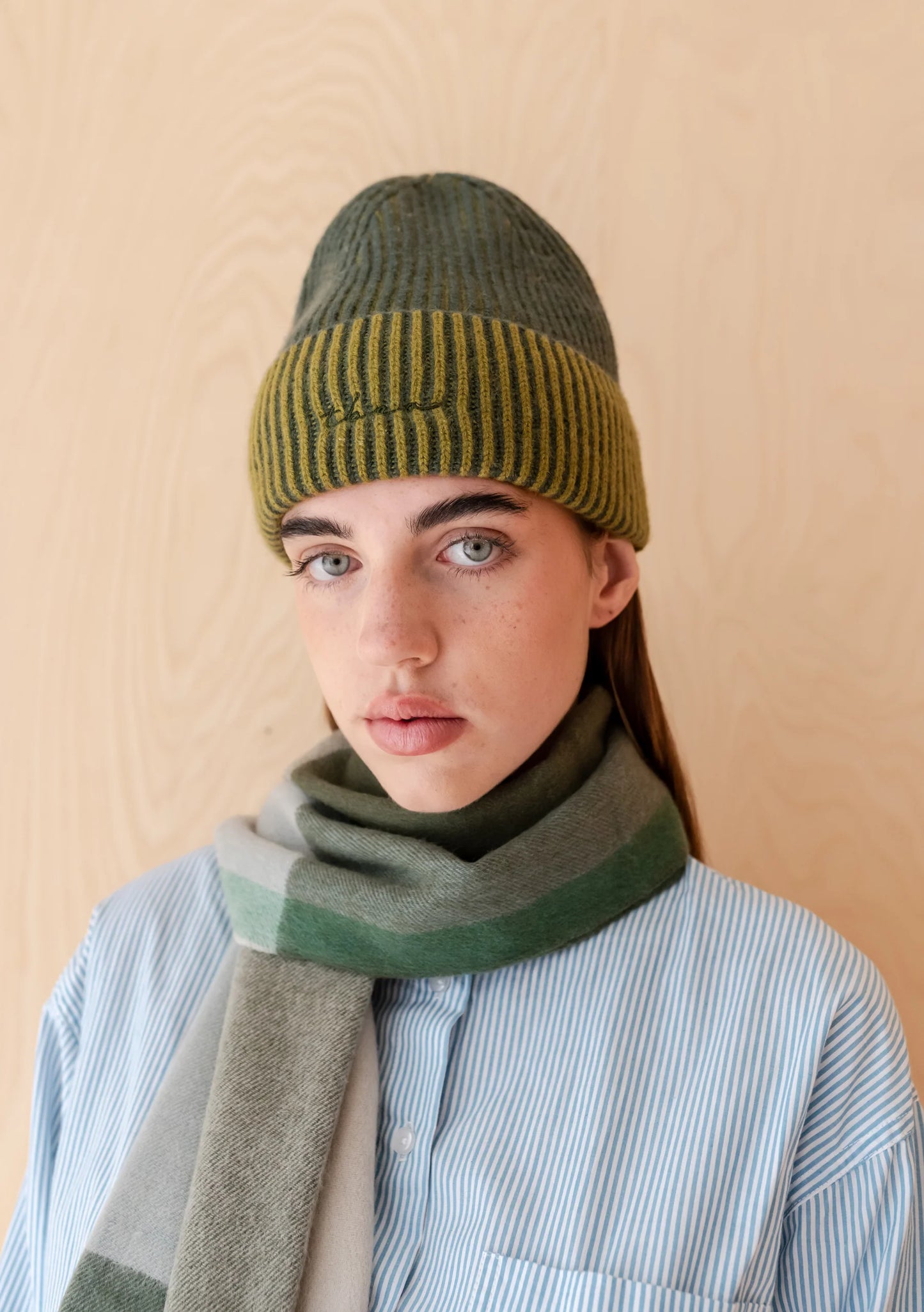 Person wearing a green knitted hat and scarf against a beige background. Hat is by TBCo and filtered for the Soft Autumn, Warm Autumn, Deep Autumn, and Warm Spring colour seasons by Shop My Palette.