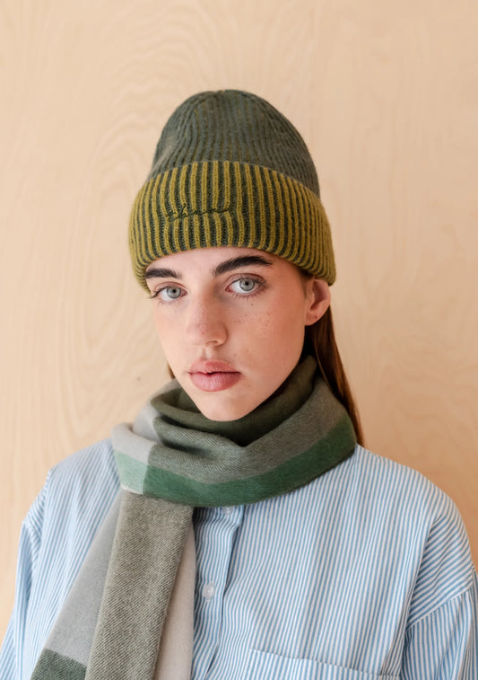 Person wearing a green knitted hat and scarf against a beige background. Hat is by TBCo and filtered for the Soft Autumn, Warm Autumn, Deep Autumn, and Warm Spring colour seasons by Shop My Palette.