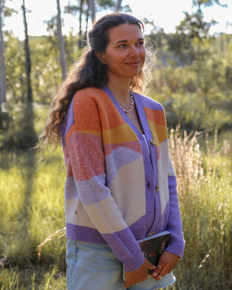 Woman wears purple and orange abstract print cardigan.