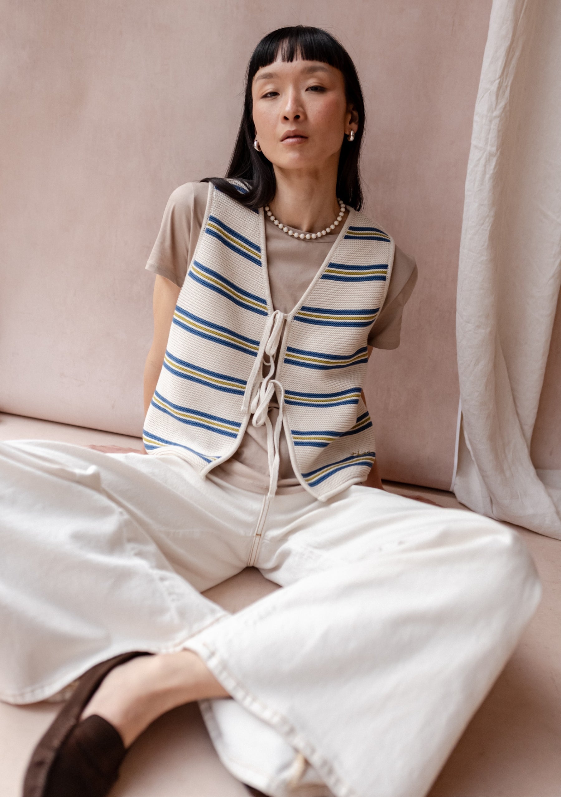 Cream striped knit sleeveless vest with blue and yellow horizontal stripes, tie-front fastening, and relaxed fit