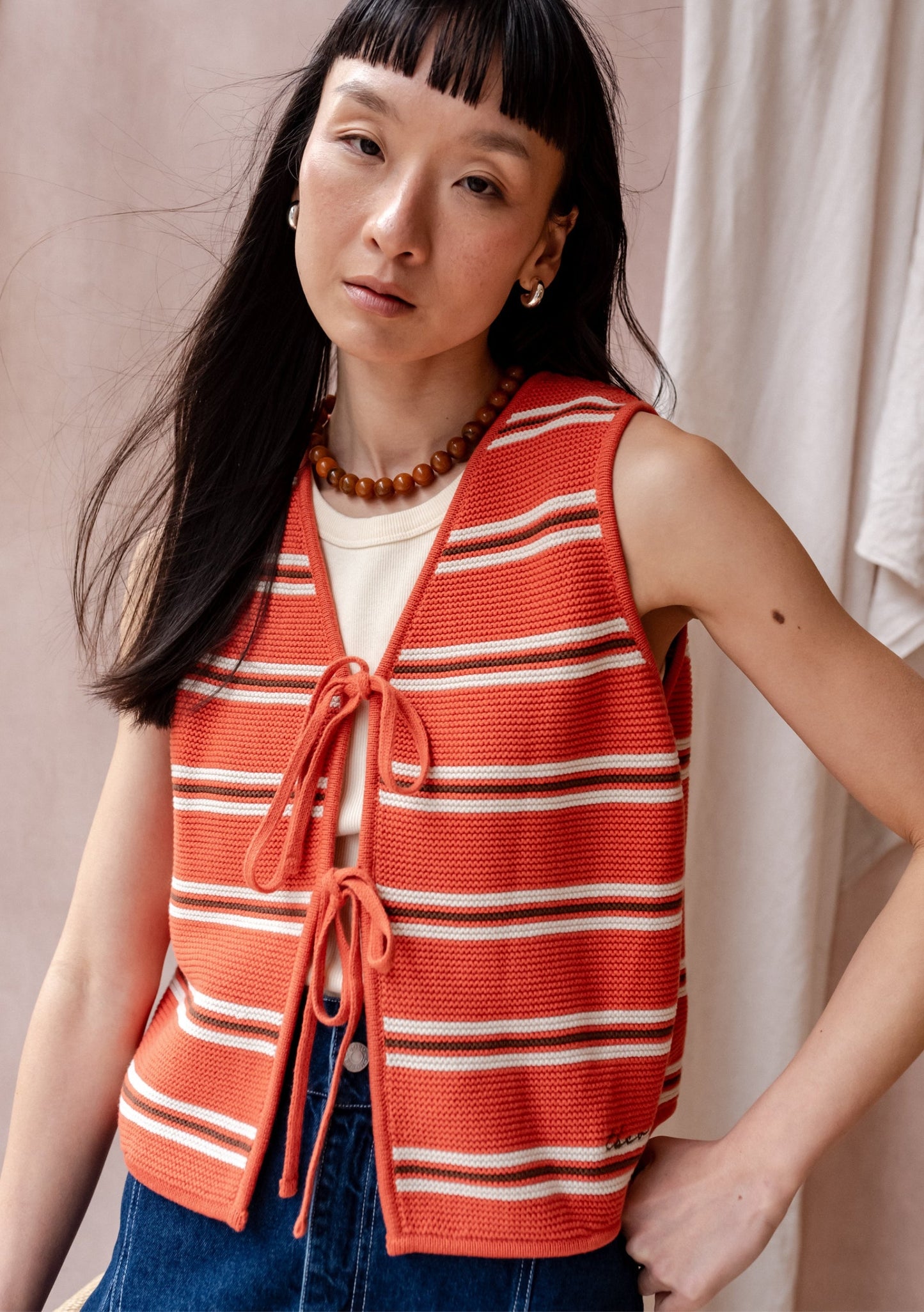 Coral orange striped knit sleeveless top with cream and brown stripes, tie-front fastening, and cropped fit
