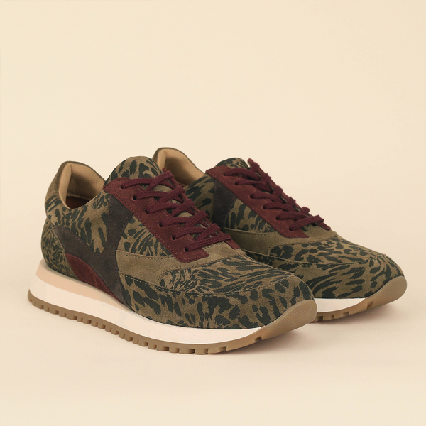 A pair of low-top trainers with an olive green and black abstract patterned upper, burgundy laces, and a thick cream midsole with a gum outsole, shown on a solid beige background.