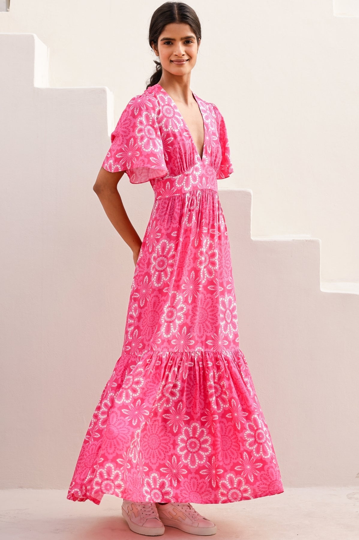 Bright pink floral maxi dress with white print, deep V-neckline, flutter sleeves, fitted waist, and tiered skirt.