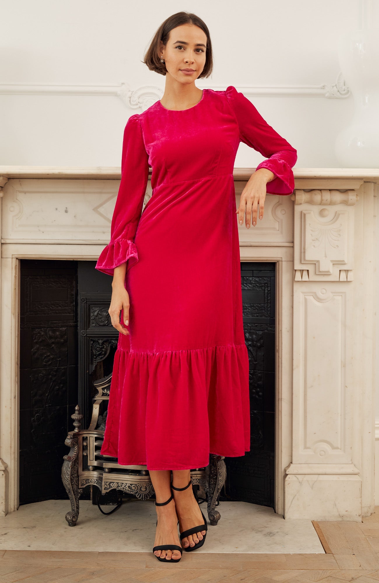 Bright raspberry velvet midi dress with round neckline, long sleeves with fluted cuffs, fitted waist seam, and gathered hem.