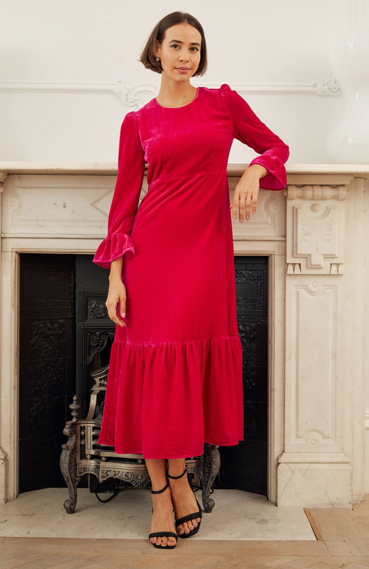 Bright raspberry velvet midi dress with round neckline, long sleeves with fluted cuffs, fitted waist seam, and gathered hem.