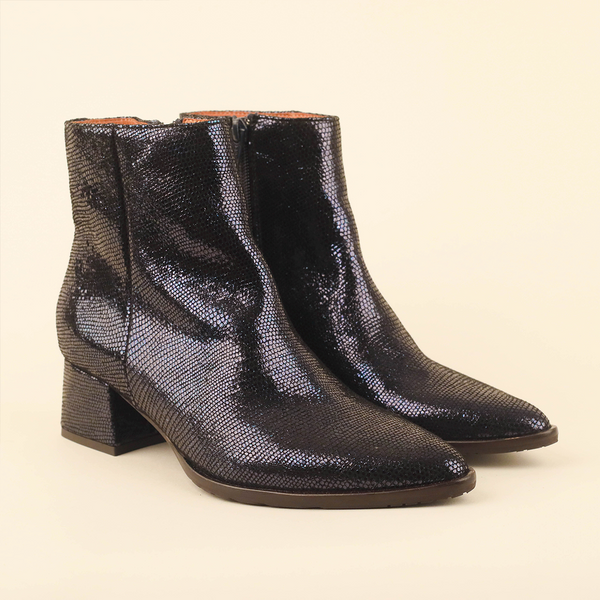 A pair of metallic navy textured ankle boots with a pointed toe and low block heel, photographed on a solid light beige background.