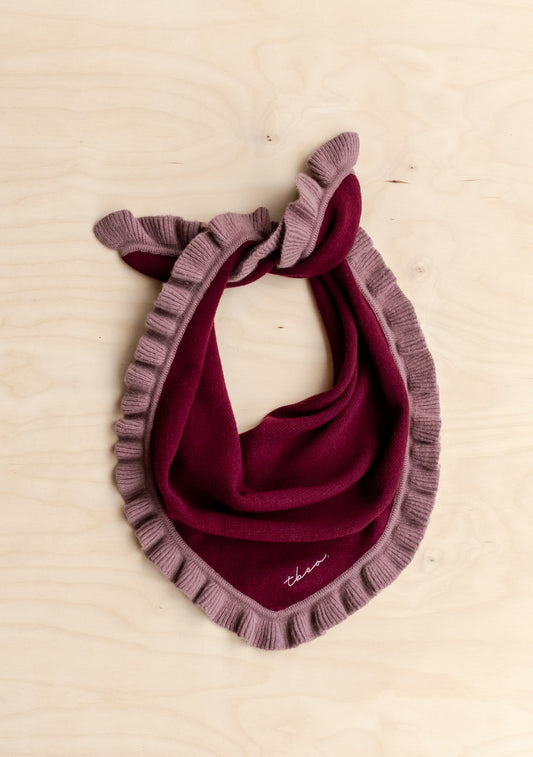 A deep burgundy merino triangle scarf with soft pink ruffle trim.