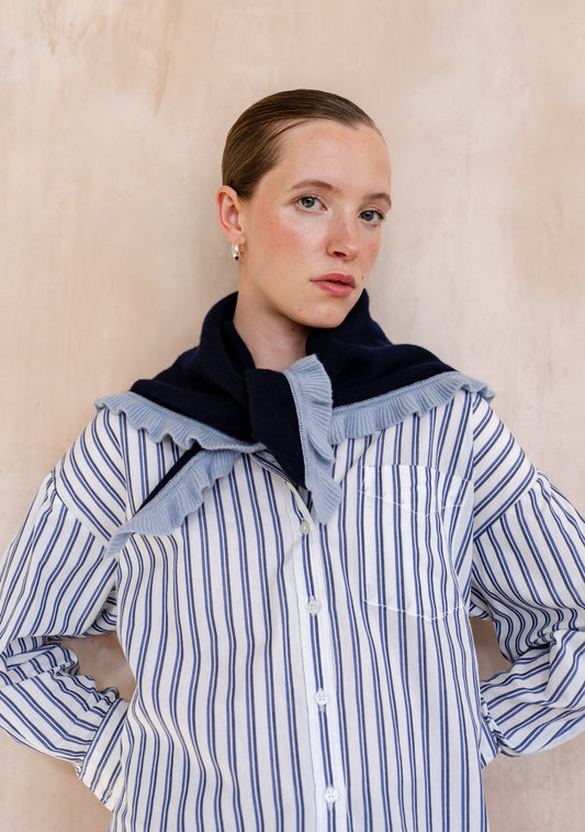 Navy scarf with light blue ruffle trim, worn tied around the shoulders over a blue and white striped shirt