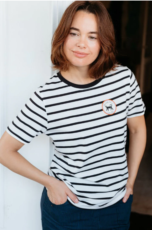 White T-shirt with black horizontal stripes, black crew neckline, and small circular badge detail on the chest