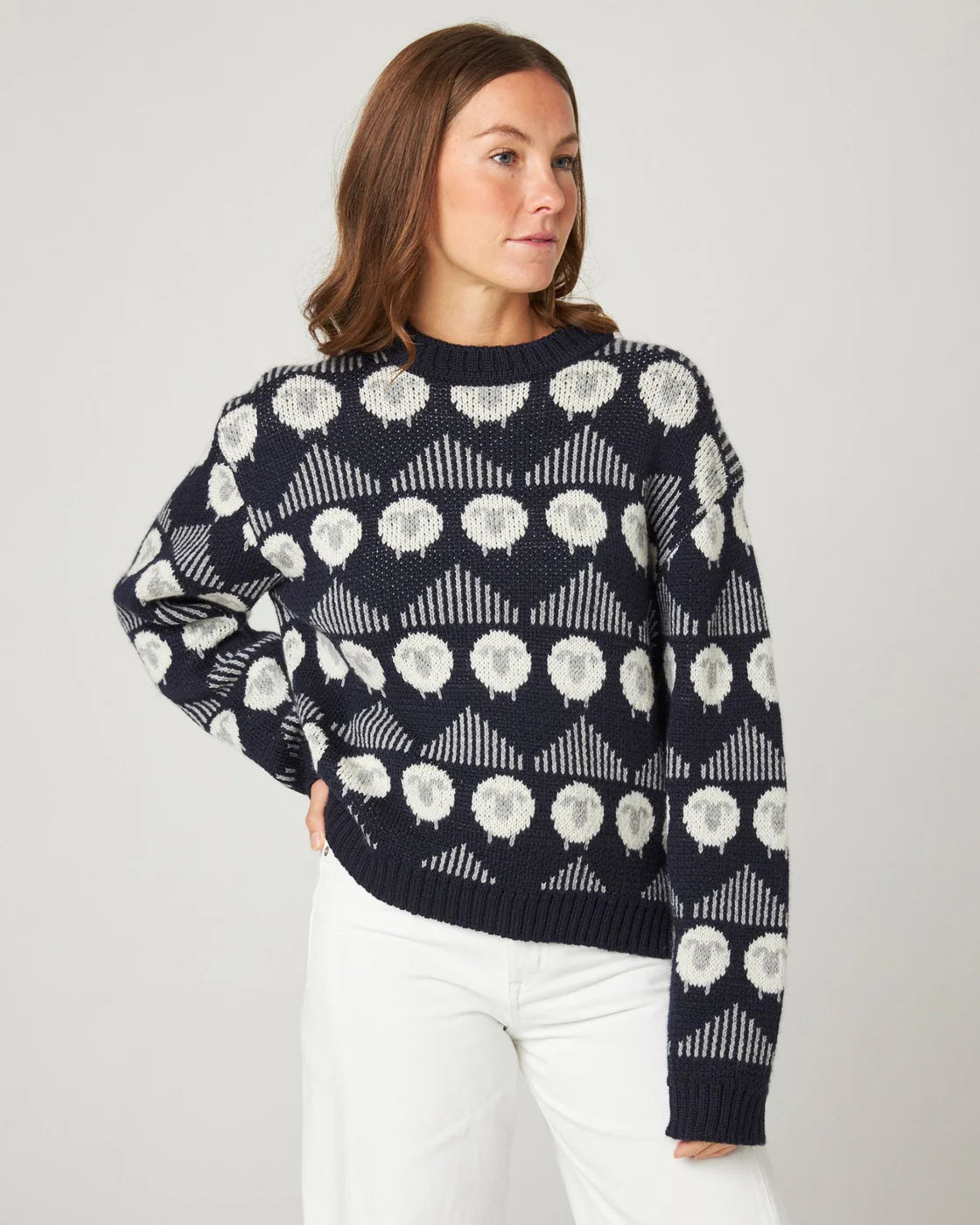 Model wearing a navy merino wool sweater with a sheep pattern by Peregrine Clothing, shown in a Deep Winter / Cool Winter-friendly colour.