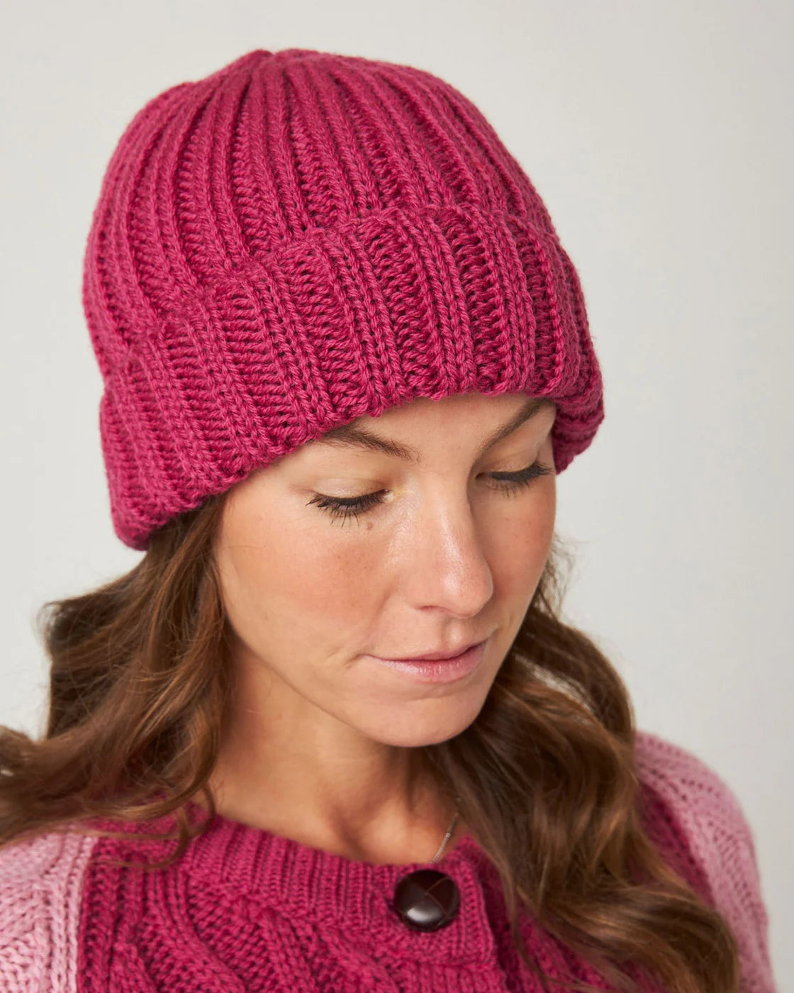 Model wears a clear fuchsia pink knitted merino wool beanie hat by Peregrine Clothing, filtered for Deep Winter, Clear Winter, and Cool Winter by Shop My Palette.