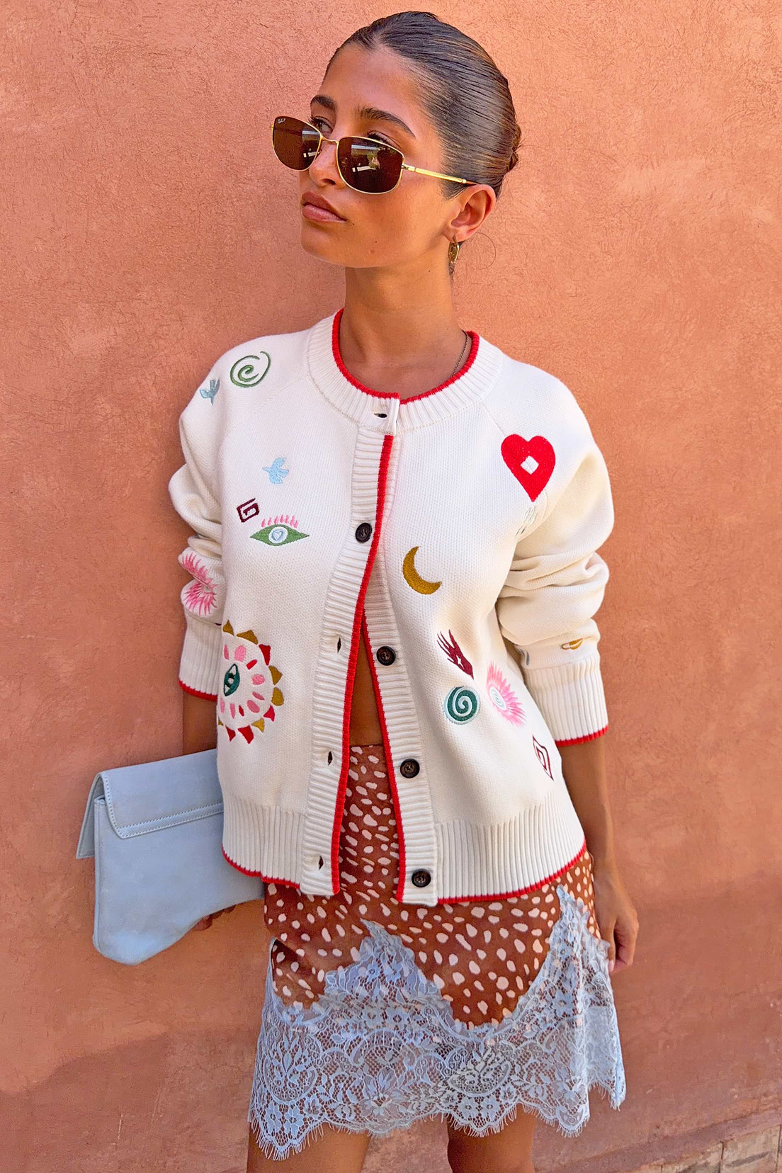 Cream cardigan with embroidered motifs and red trim.
