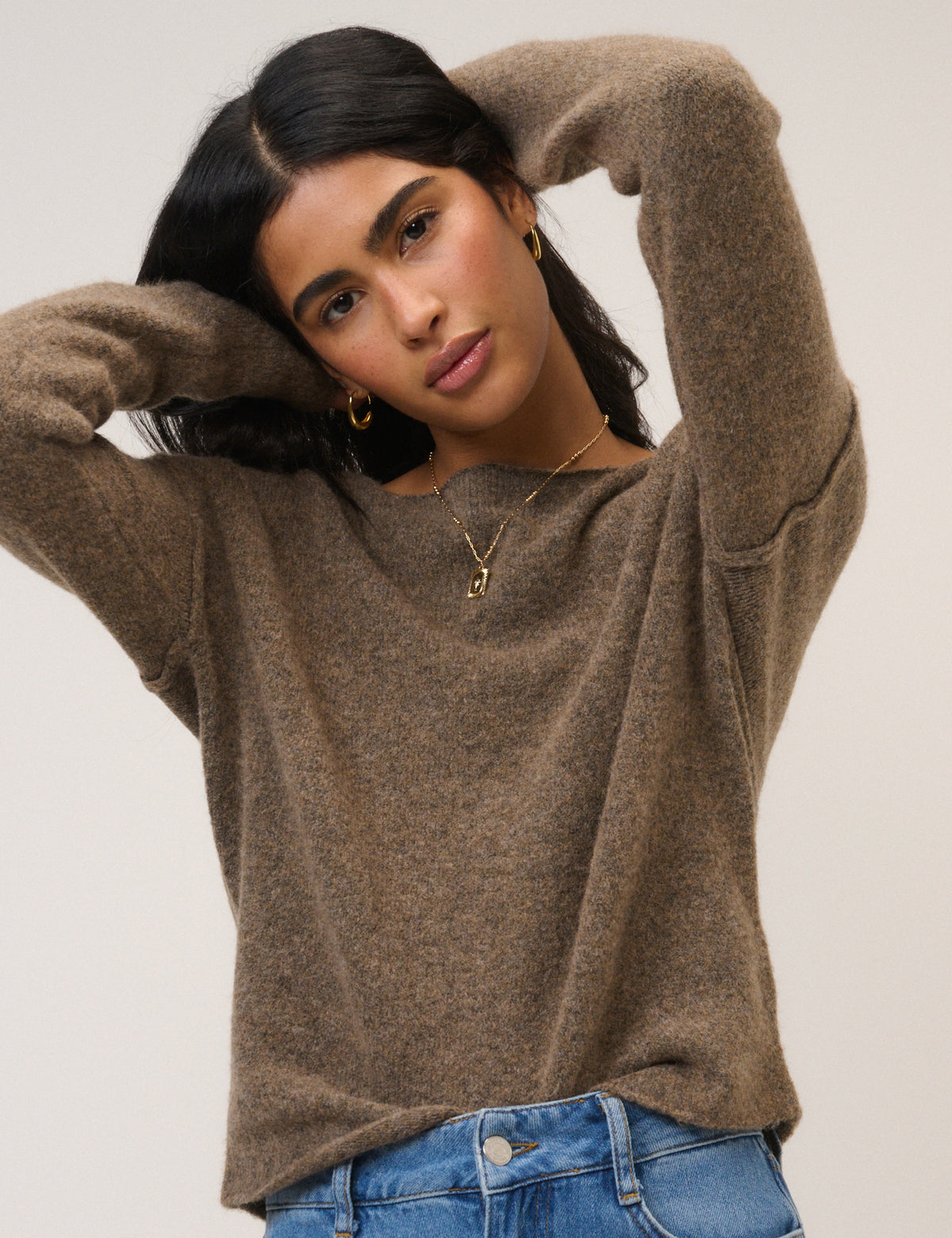 Woman wearing a brown jumper and blue jeans against a plain background