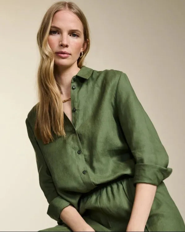 Woman with blond hair, wearing a khaki green linen outfit perfect for Autumn season, against a beige background.