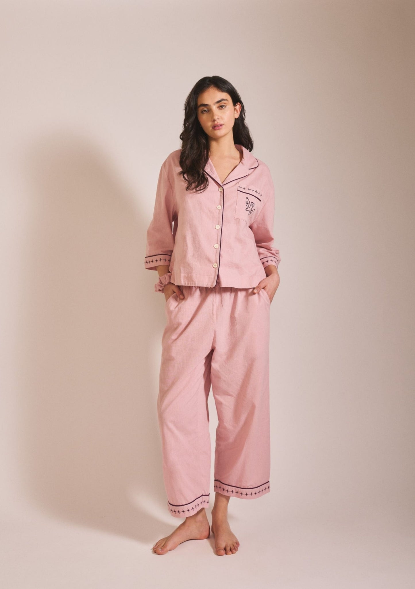 Model wearing a relaxed-fit pink pyjama set in a soft, muted dusty rose tone, with long sleeves, button front, and loose trousers.