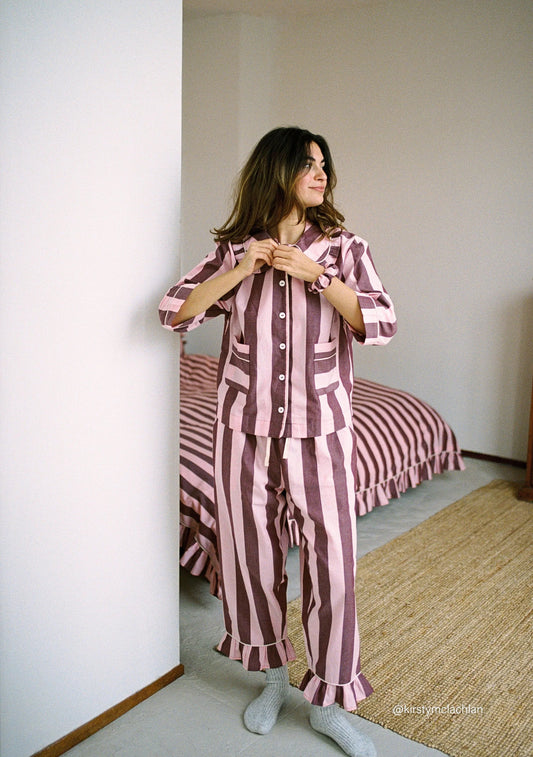 Woman wearing a burgundy and lilac striped pyjama set in a bedroom. Pyjamas are by TBCo and are filtered by Shop My Palette for the Cool Summer, Soft Summer, and Light Summer colour seasons.