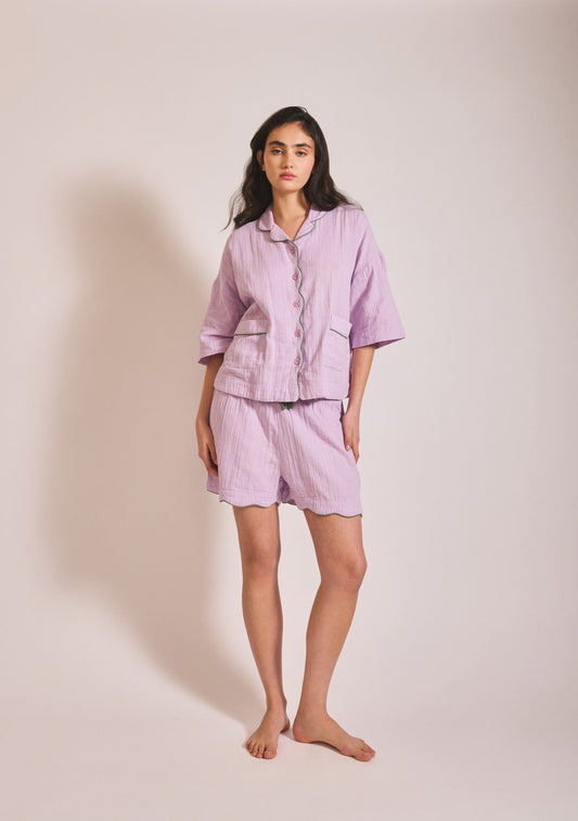 Relaxed lilac cotton pyjama set with button-up top, loose fit, and cropped trousers with scalloped hem detailing.