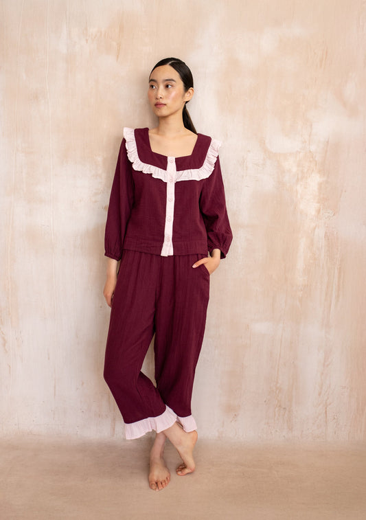Burgundy pyjama set with soft pink trim, featuring a button-up top with ruffled neckline and matching trousers with ruffle hem.